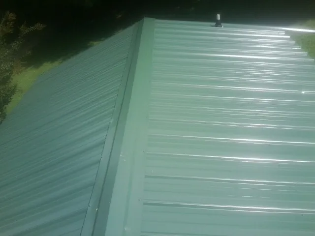New green metal panels meeting at the ridge of a roof — Flat Roof Repair work by our crew in Lucas