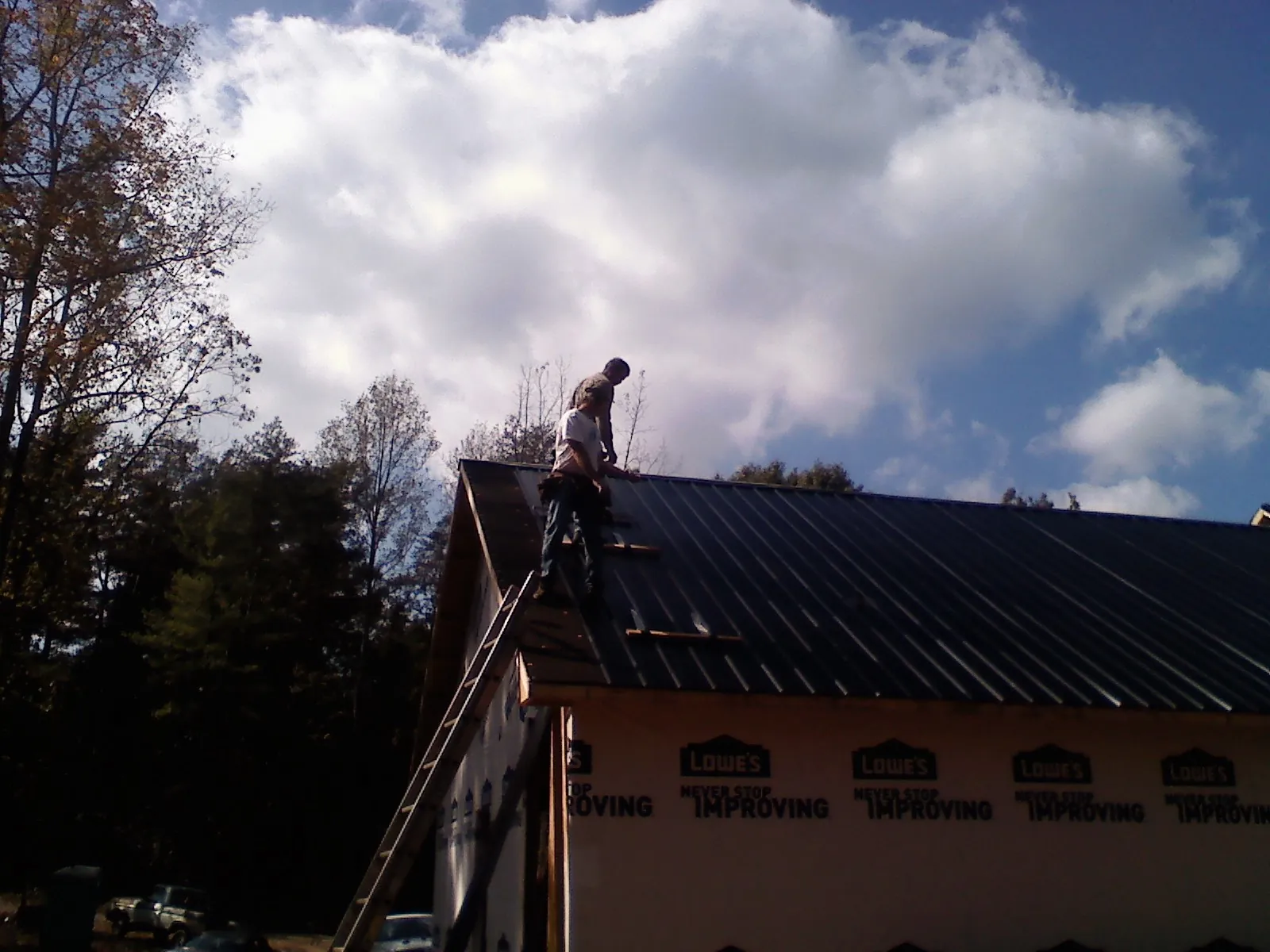 Roofer fastening dark metal panels high against a cloudy sky, from a Roof Inspection job in Lucas