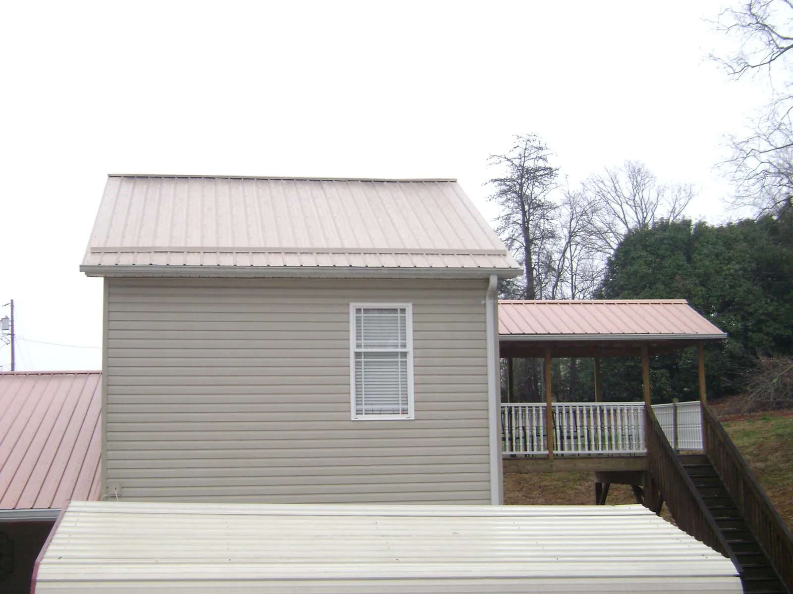 Tan metal roofs on a two story addition and attached porch, from a Roof Replacement job in Lucas